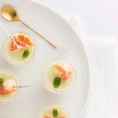 Delicioso chupito de melón con jamón serrano y menta, servido en copas pequeñas con una cuchara dorada.