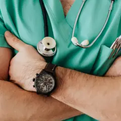 Medico con camice verde, stetoscopio e orologio, pronto ad ascoltare. La sua espressione suggerisce un'attenta valutazione, forse in vista di una **denuncia medico di base**.