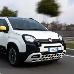 Nuova Fiat Panda GPL in movimento su strada. L'auto bianca con dettagli neri e specchietti gialli sfreccia con un'icona verde GPL in primo piano.