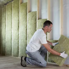 Un ouvrier installe un panneau d'isolant thermique dans une structure murale en bois.