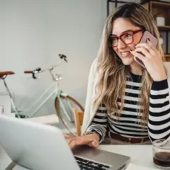 Frau am Telefon, lächelnd, am Laptop arbeitend. Hinter ihr ein Fahrrad. Perfekt für den **iu semesterbeginn**-Stress.