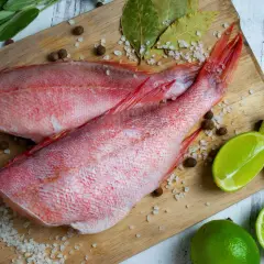 Dwa surowe karmazyny na desce, przygotowane do pieczenia. Obok limonki, chili, ziele angielskie i sól. Idealny karmazyn przepis na obiad.