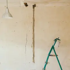 Pękające ściany starego domu, widoczna instalacja elektryczna i drabina.