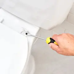 A hand uses a screwdriver to tighten a bolt, demonstrating how to install a toilet seat.
