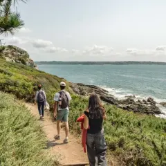Trois randonneurs explorent un sentier côtier verdoyant, le **gr 34**, face à la mer d'un bleu profond.