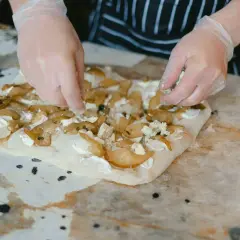 Manos enguantadas añaden queso azul a una focaccia con peras. Una deliciosa focaccia reteta en proceso.