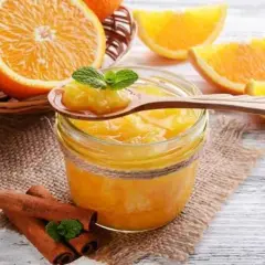 Tarro de mermelada de naranja casera, con naranjas frescas y canela en rama. Una cucharada muestra la textura.