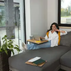 Kobieta na kanapie rozmawia przez telefon, pracując na laptopie. To idealne miejsce do znalezienia najlepszej umowy najmu mieszkania.