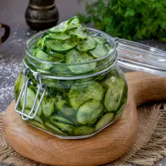 Barattolo di vetro pieno di fette di cetrioli in agrodolce, con aneto e sale sparso.