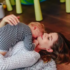 Mama i dziecko leżą na podłodze. Dziecko przytula się do mamy. To piękny przykład, co to stymulacja rozwoju poprzez bliskość i zabawę.