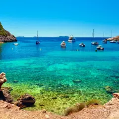 Aguas cristalinas en cala salinas, con barcos anclados y una costa rocosa y verde.