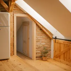 Jasny, kremowy lodówka Smeg, drewniane drzwi przesuwne i ceglana ściana na poddaszu.