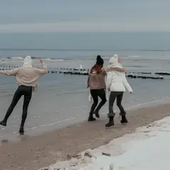 Trzy dziewczyny cieszą się zimą nad morzem, spacerując po zaśnieżonej plaży. Wesoła atmosfera i zimowy krajobraz.