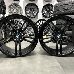 Dwa czarne felgi BMW z logo, idealne do tuningu. W tle inne felgi i opony.