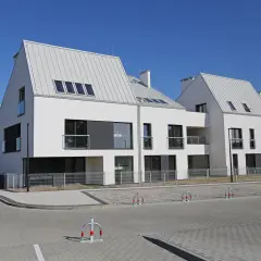 Nowoczesne domy szeregowe z białymi elewacjami i szarymi dachami tworzą malowniczą panoramę osiedla.