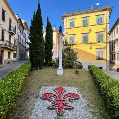 Fivizzano cosa vedere: un'aiuola con un giglio rosso e un monumento in un vicolo con case colorate.