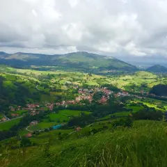 Paisaje verde y montañoso, con un pueblo en el valle. La **ruta Tetas de Liérganes** ofrece vistas espectaculares.