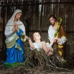 Święta Rodzina w żłóbku. Maryja w błękitnej sukni, Józef w brązowym płaszczu i biała szata Dzieciątka Jezus.