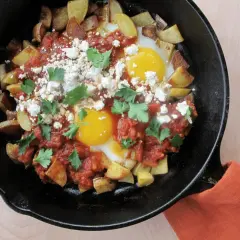 Plat savoureux : recette pomme de terre oeuf avec sauce tomate, fromage émietté et persil frais, servi dans une poêle en fonte.