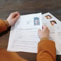 Osoba przegląda dokumenty CV z portretami.