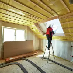 Lavoratore su scala installa isolamento giallo nel sottotetto, una scelta chiave per capire se meglio isolare il tetto o il sottotetto.