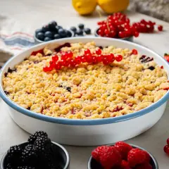 Ein köstlicher Beeren Crumble mit roten Johannisbeeren, Blaubeeren und Himbeeren, garniert mit frischen Beeren und Zitronenspalten.