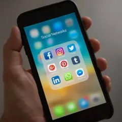 Dłoń trzyma smartfon z ikonami mediów społecznościowych. Idealne narzędzia dla każdego social media managera do zarządzania profilami.