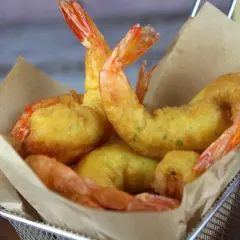 Crujientes gambas a la gabardina doradas, servidas en una cesta metálica con papel marrón.