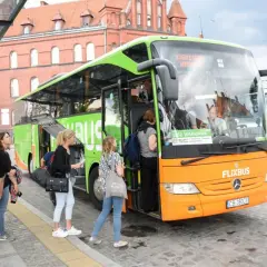 Pomarańczowo-zielony autobus FlixBus na przystanku, pasażerowie wsiadają.