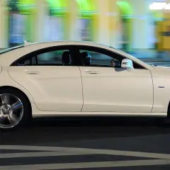 Biały Mercedes CLS 63 AMG mija nocą rozmyte światła miasta, jego sylwetka jest dynamiczna i elegancka.