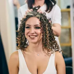 Une femme souriante se fait faire une permanente chez le coiffeur. Ses cheveux bouclés sont magnifiques.