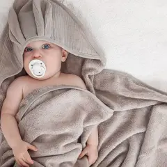 Uroczy niemowlak z niebieskimi oczami i smoczkiem, otulony miękkim, szarym ręcznikiem kąpielowym dla niemowląt.