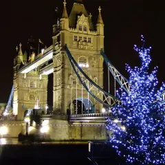 Albero di Natale illuminato con luci blu davanti al Tower Bridge di Londra, evocando l'atmosfera dei mercatini di Natale in inglese.