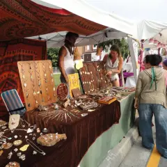 En el **mercado hippie Argaños**, se exhiben collares y pulseras artesanales. Una vendedora muestra su mercancía a dos clientas.