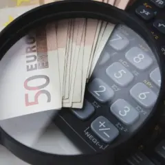 Lupe über 50-Euro-Scheinen und einem Taschenrechner. So wird die Frage "wie viel verdient man im Referendariat" visuell beleuchtet.