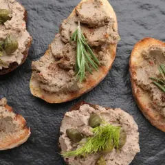 Pyszny pasztet z mięsa z rosołu na grzankach, ozdobiony kaparami, koperkiem i rozmarynem. Idealna przekąska.