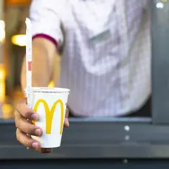 Ręka podaje kubek z McDonald's. Zastanawiasz się, ile kalorii ma cola zero z McDonald's? Ten napój ma zero kalorii.
