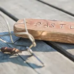 En träbit med texten "BASTU" och en metallskopa ligger på en träbrygga. Kanske en påminnelse om en härlig stund på Östholmen bastu.