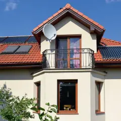 Dom z balkonem i oknami, na dachu kolektory słoneczne. Czy to wykusz co to? Tak, to element architektoniczny.