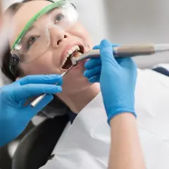 Pacjentka w okularach ochronnych uśmiecha się, gdy dentysta wykonuje zabieg. Nowoczesne znieczulenie komputerowe zapewnia komfort.