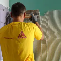 Operaio con maglia gialla Sika applica colla per incollare piastrelle su piastrelle parete.