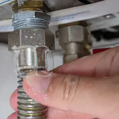 Burbujas de agua saliendo de una conexión de caldera, tocada por un dedo.