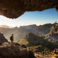 Una persona con mochila admira el paisaje montañoso al amanecer, disfrutando de unas increíbles caminatas Gran Canaria.