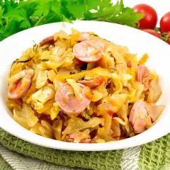 Młoda kapusta z kiełbasą, duszona z pomidorami i ziołami, podana na białym talerzu.