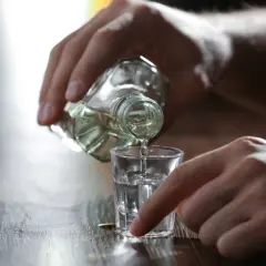 Dłoń nalewa alkohol do kieliszka. Może to być pierwszy kieliszek wypity na czczo.
