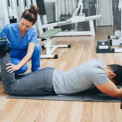 Fizjoterapeutka pomaga pacjentowi w ćwiczeniach kinezyterapii, wykorzystując sprzęt do rehabilitacji.