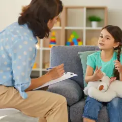 Psycholog rozmawia z dzieckiem, które trzyma misia.