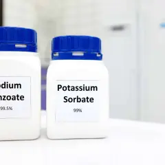 Zwei weiße Behälter mit blauen Deckeln stehen nebeneinander. Auf dem linken Behälter steht "Sodium Benzoate 99.5%", auf dem rechten "Potassium Sorbate 99%".