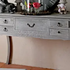 Console grise patinée, ornée de motifs floraux sculptés. Ce meuble à tiroirs, idéal pour un intérieur cosy, invite à y poser des objets décoratifs.