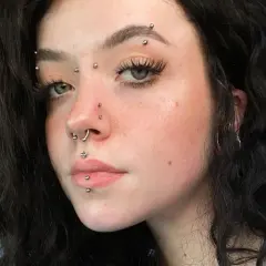 Młoda kobieta z wieloma kolczykami, w tym kolczyk w brwi, septum i wargach.